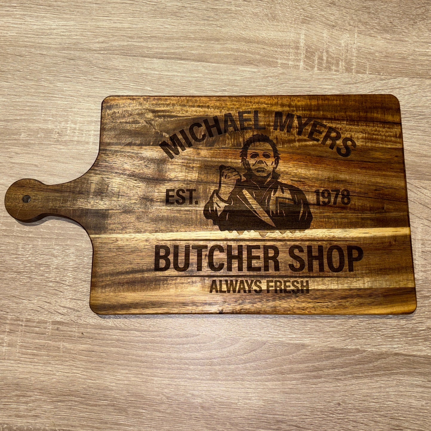 Wooden cutting board with engraved text and a photo of a person on a wooden surface