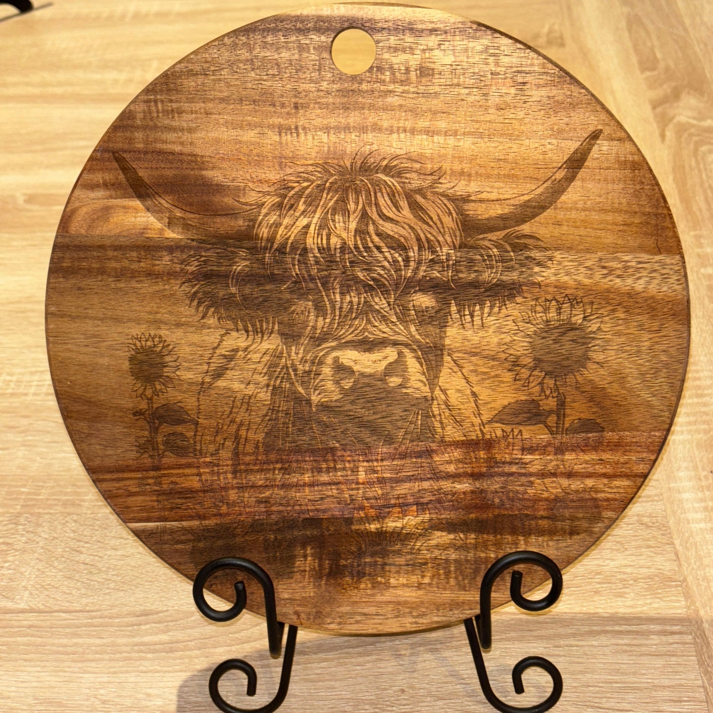 Wooden cutting board with engraved bull design on a wooden stand.