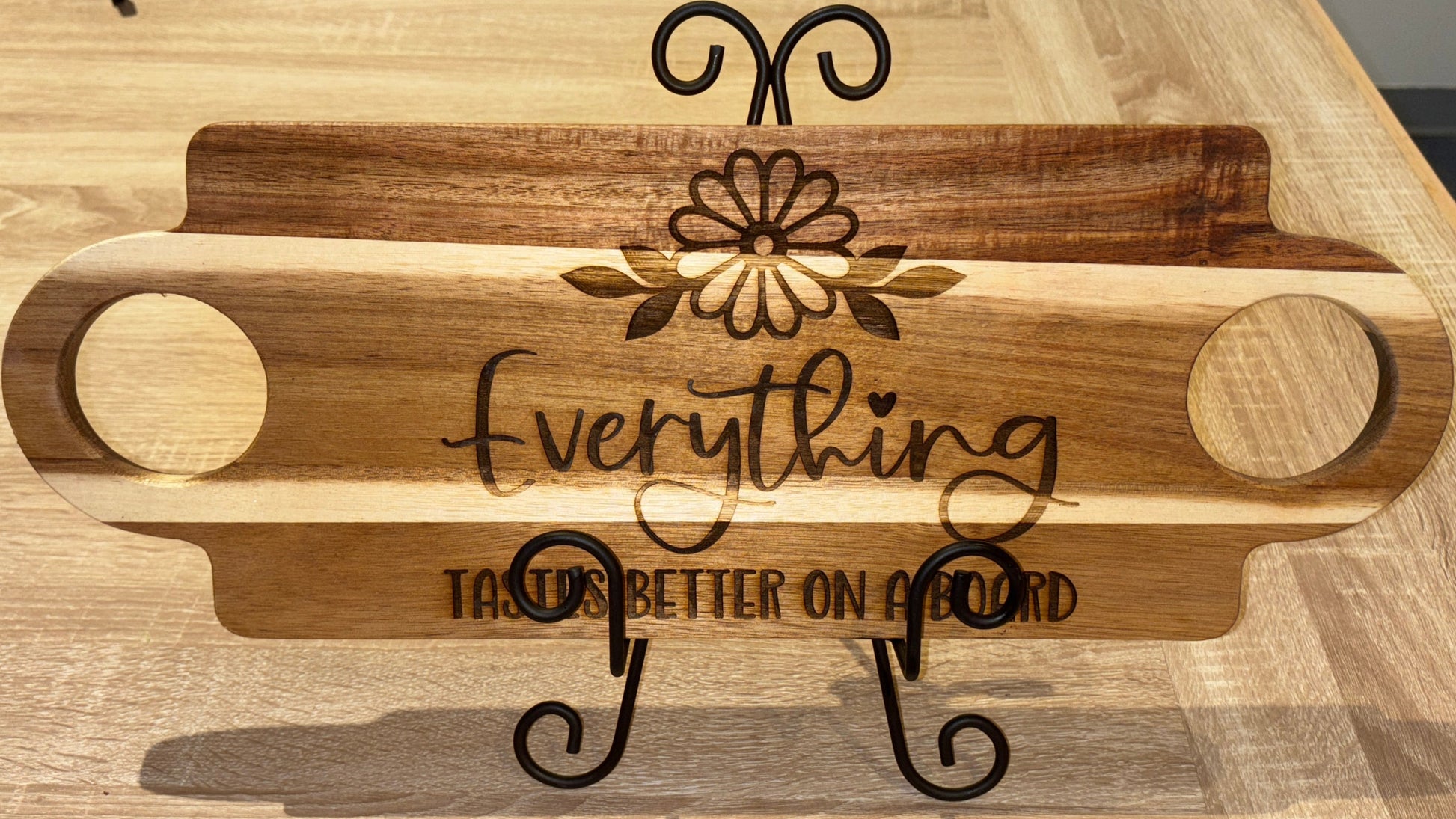 Wooden serving board with decorative double handle and engraved text on a wooden surface.